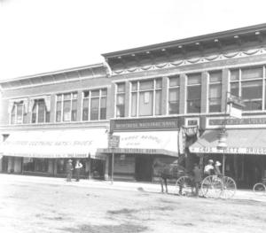View along Main Street in early Montrose (between 1905 and 1915). Shows a horse-drawn carriage, bicycles, and two men talking. Signs include: "The Humphries  Mercantile Co. Dry Goods, Clothing, Hats & Shoes" "Montrose National Bank" and C. J. Getz, Pharmacist, Druggist." via http://photoswest.org