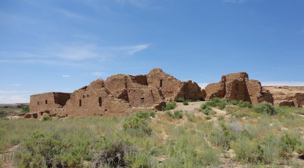 Ancient stone ruins surrounded by desert vegetation under a blue sky.