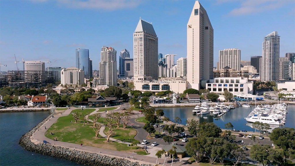 Aerial view of San Diego's skyline featuring modern skyscrapers, a marina with docked boats, and a park along the waterfront.