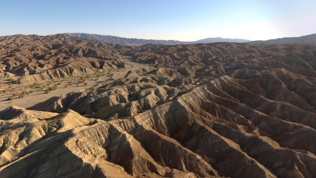 Aerial view of rugged brown mountains and valleys under a clear sky, showcasing a desert landscape.