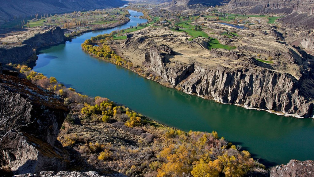 Aerial view of a winding river surrounded by rocky cliffs and vibrant autumn foliage.