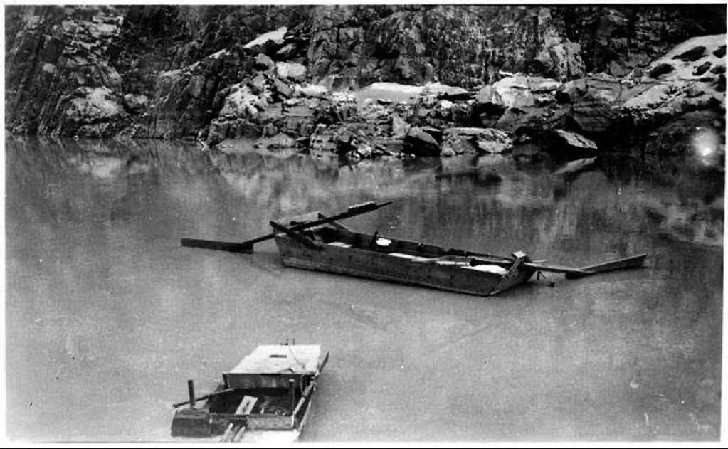 Black and white photo of two small boats floating on a calm body of water, surrounded by rocky cliffs.