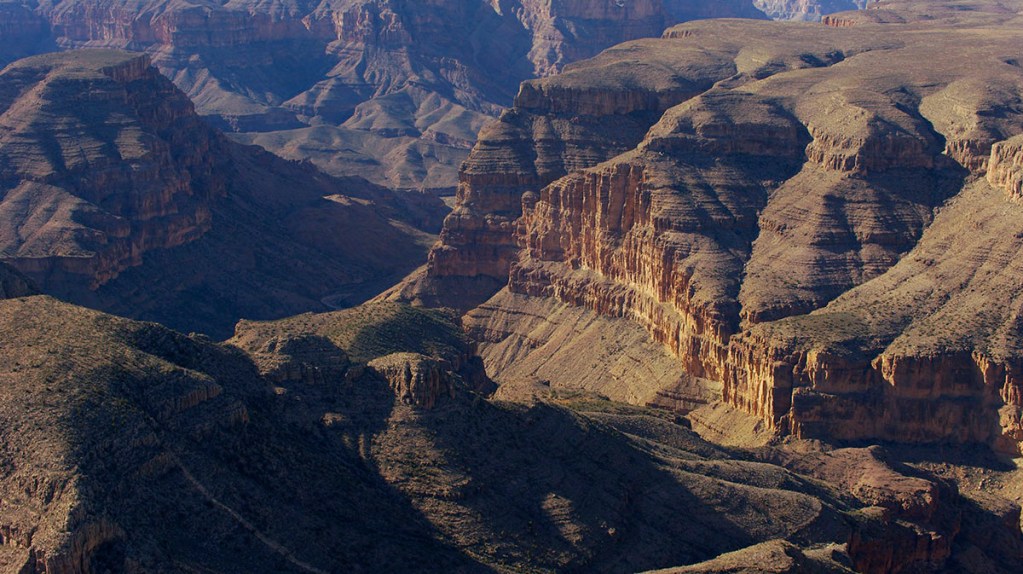 A panoramic view of the Grand Canyon showcasing its steep rock formations and layered cliffs under a clear sky.
